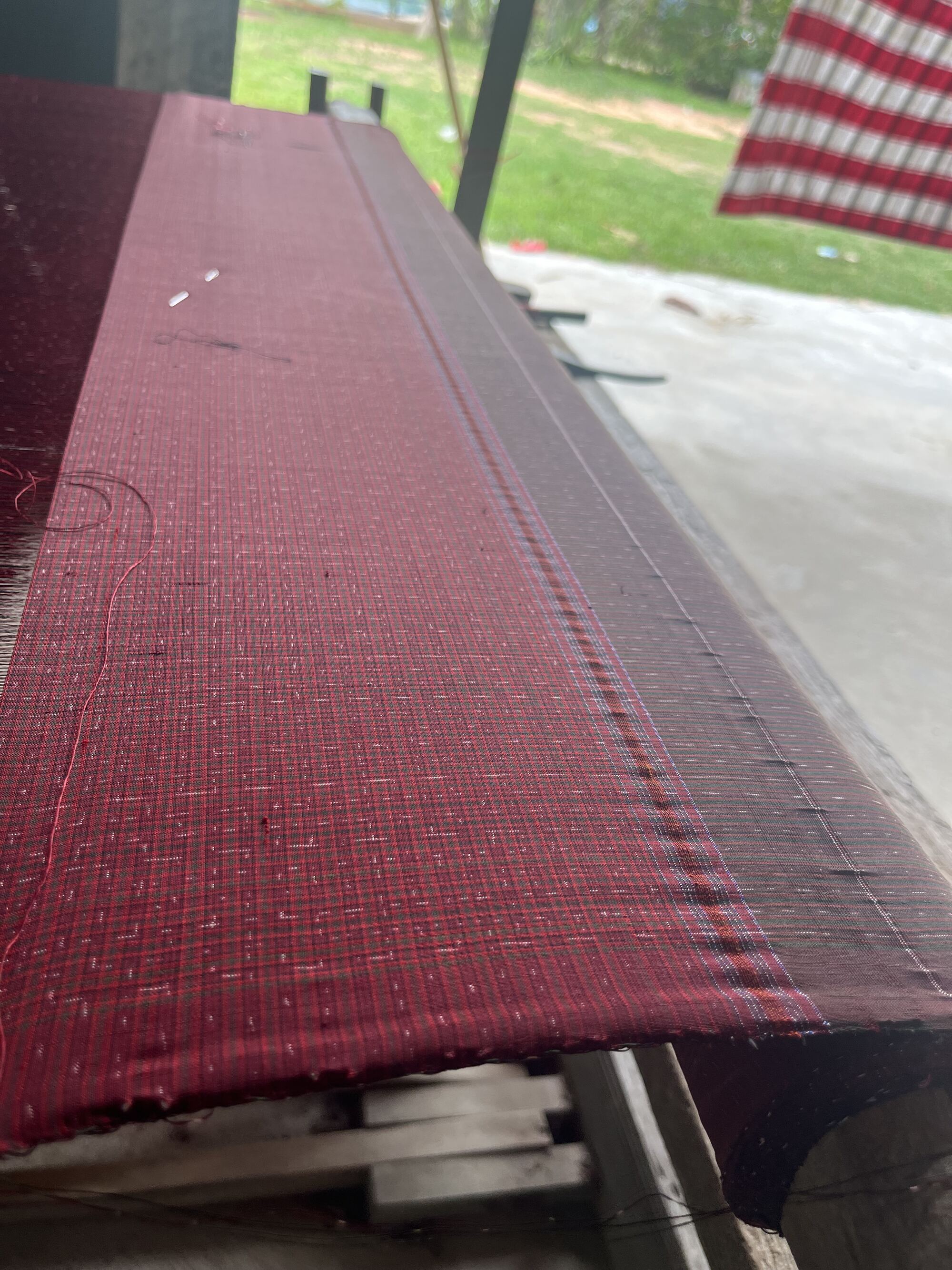 A length of deep red silk stretched on the wooden loom in the shade under the house