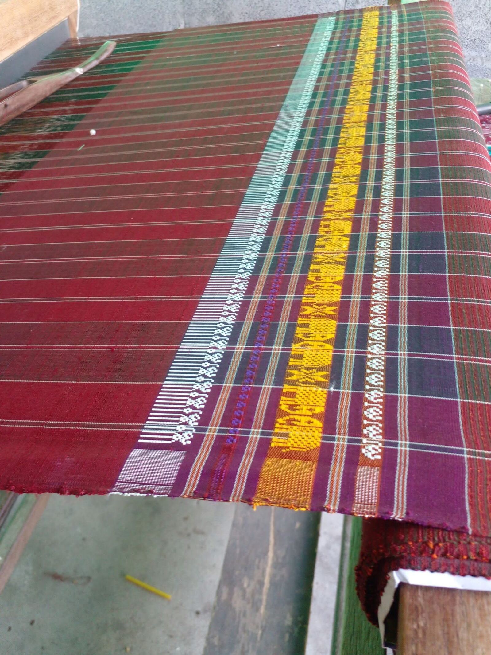 A finished sabai in reds and golds still on the loom, its elephant border catching the light